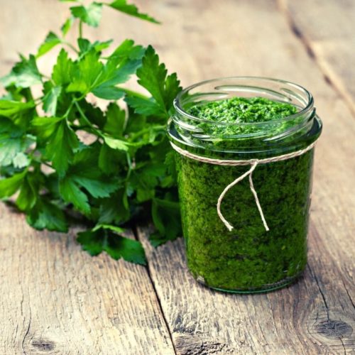 parsley pesto in a mason jar on a wood table with a bunch of parsley