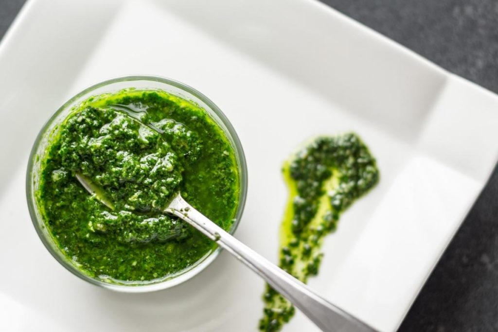 oregano pesto sauce in a jar with a spoon on a white plate