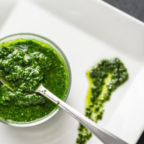 oregano pesto sauce in a jar with a spoon on a white plate